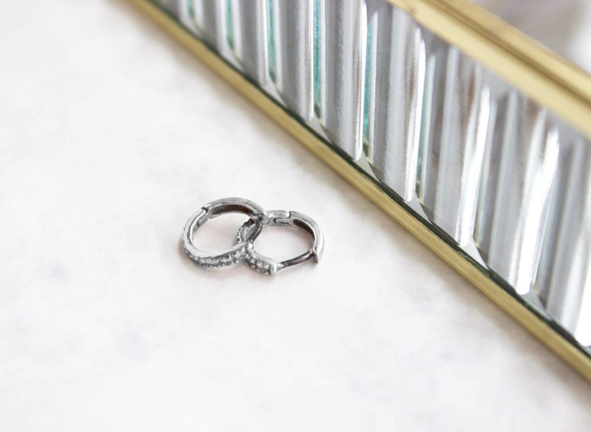 Two tarnished sterling silver huggie hoop earrings on a marble surface