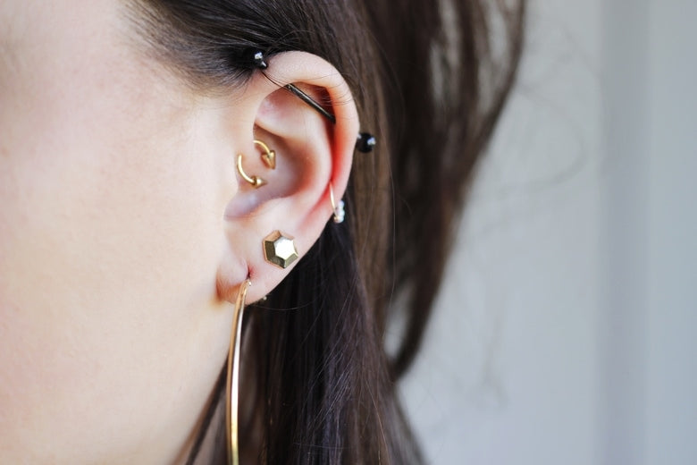 Ear with an industrial bar, small gold cartilage rings, a gold lobe stud and a large gold hoop